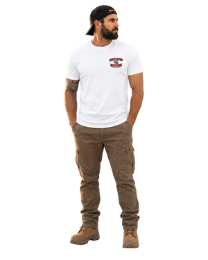 A man modeling a white crewneck t-shirt with a small red and blue chest graphic, paired with brown cargo pants and brown boots, standing against a light gray studio background.