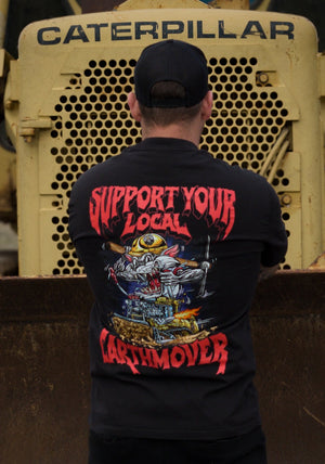 Person wearing a black t-shirt with 'Support Your Local Earthmover' design in front of a Caterpillar machine.