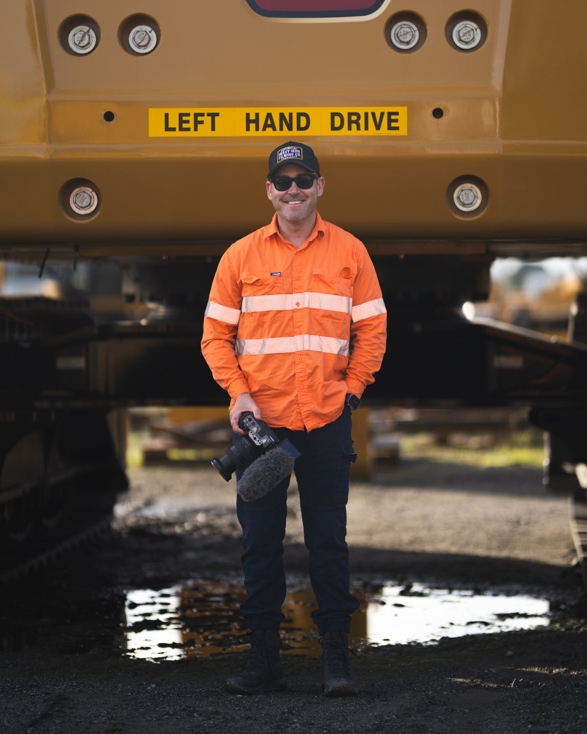 Brad from Earthmoving Downunder holding his camera in front of a CAT machine on a worksite