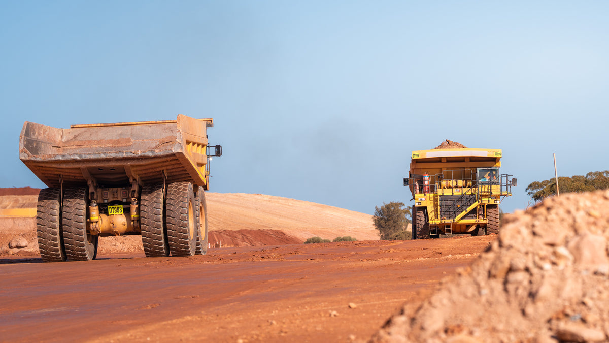 Two CAT mining haul trucks travelling along a red dirt road, photographed by Earthmoving Downunder