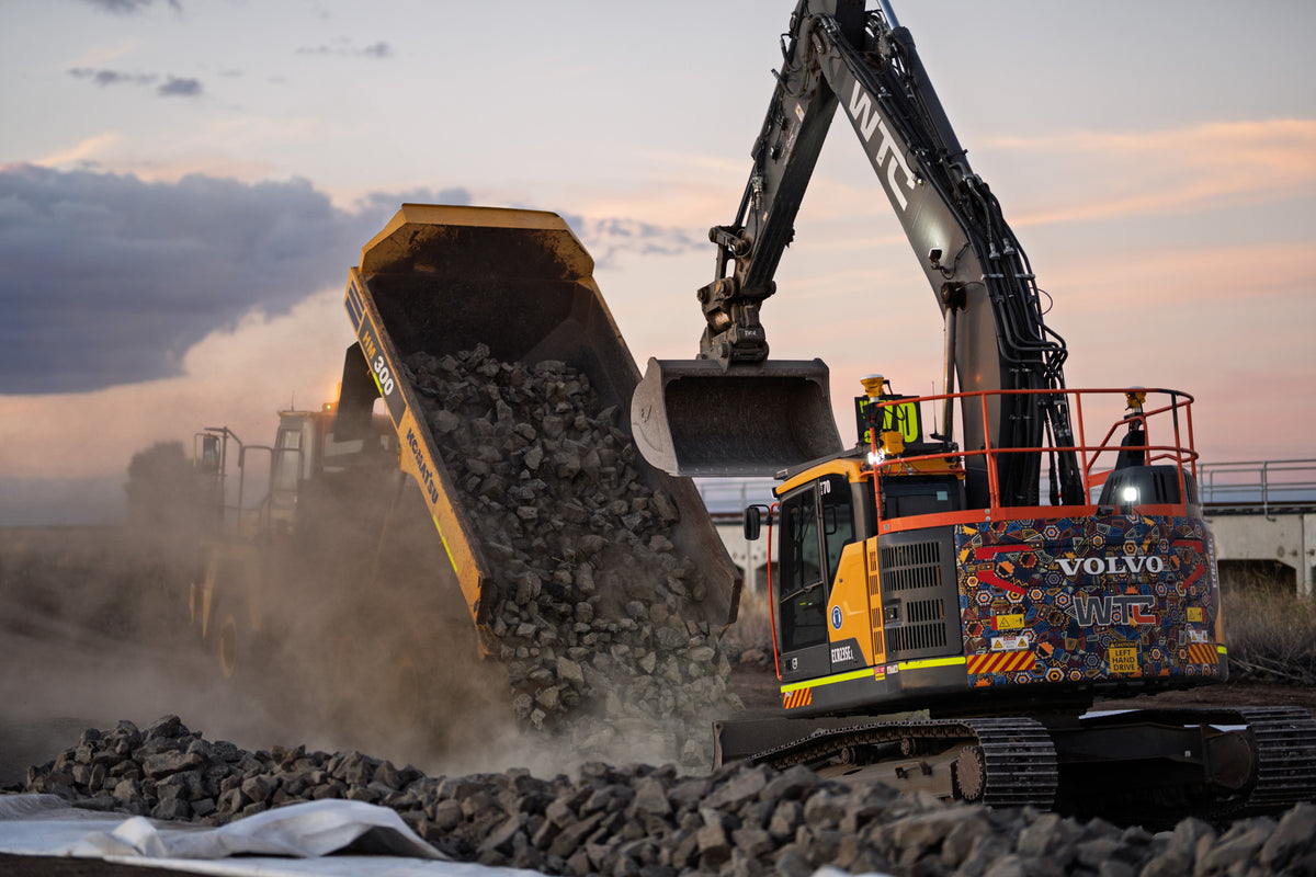 Volvo excavator and Komatsu articulated dump truck moving rock at sunset, photographed by Earthmoving Downunder